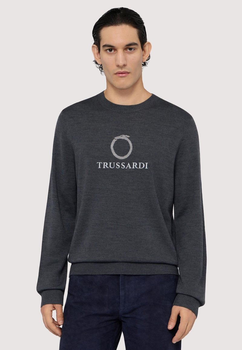 Mörkgrå stickad tröja med långa ärmar, rund halsringning och TRUSSARDI-logotyp i ljusgrått. Ribbad mudd och fåll. Mjuk textur.