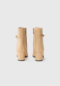 Beige leren enkelboots met een gladde afwerking, vierkante hakken en decoratieve banden. Voorzien van een ritssluiting aan de achterkant.