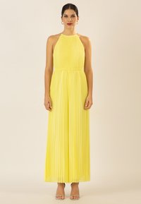 Robe maxi plissée jaune avec un décolleté halter, une taille élastique et une silhouette fluide. Associée à des talons argentés à lanières.