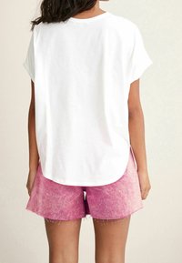 Hvid kortærmet t-shirt med rund søm, parret med lyserøde denimshorts med en råkant og en falmet tekstur.