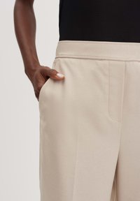 Beige op maat gemaakte broek met een gladde voorkant, zijzakken en een soepele stoftextuur, met een nette taillebandontwerp.
