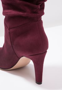 Bottine bordeaux à talon haut avec une texture en daim, bout pointu, design décontracté et talon stiletto fin.
