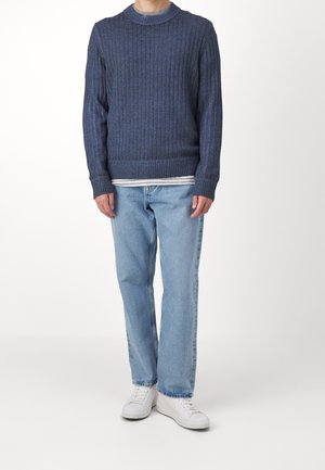Dunkelblauer gerippter Pullover mit Rundhals, kombiniert mit hellblauen geraden Jeans und weißen Sneakern.