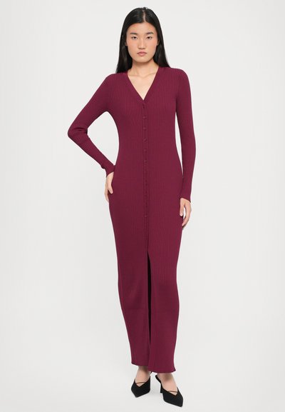 Burgundy, ribbed, long-sleeve dress with a deep V-neck, button front, and front slit. Soft, textured fabric, fitted silhouette.