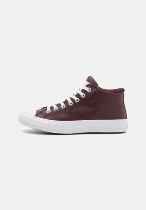 Basket montante en cuir marron foncé avec semelle en caoutchouc blanche et lacets blancs, vue de côté sur un fond clair.