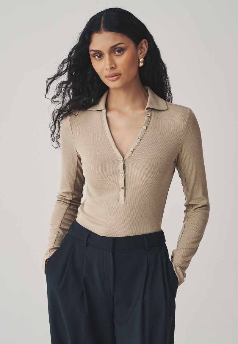 Top polo beige de manga larga con textura acanalada, escote en v y cierre de botones, combinado con pantalones azul marino de tiro alto. Textura suave y diseño ajustado.