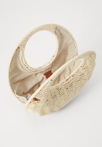 Woven natural straw handbag with circular handles, beige fabric lining, and a solid base. Features a small leather logo accent.