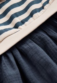 Un tissu rayé beige et marine rencontre une bande côtelée beige au-dessus d'un tissu texturé bleu marine foncé froncé.