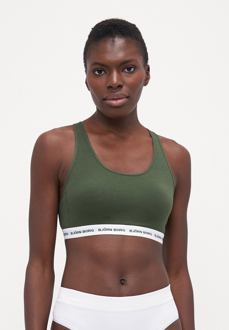 Soutien-gorge de sport vert olive avec un design racerback, en tissu doux, et une bande élastique blanche marquée en bas. Sans rembourrage, forme ajustée.