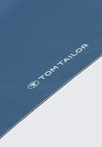 Blauwe stof met een gladde textuur, voorzien van witte stiknaden en het "TOM TAILOR"-logo. Het ontwerp heeft een strakke, minimalistische stijl.