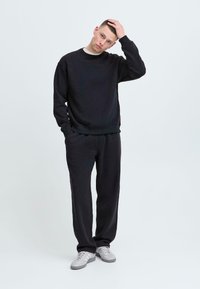 Set di felpa nera e pantaloni della tuta, realizzato in tessuto morbido. L'insieme presenta una vestibilità comoda, polsini a coste e un design minimalista.