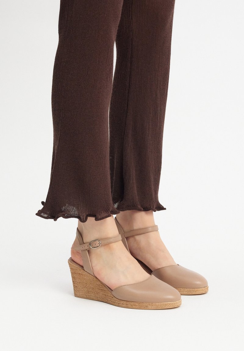 Sandales compensées en cuir beige avec un bout arrondi, une bride de cheville dotée d'une boucle argentée et une semelle espadrille tissée et texturée.
