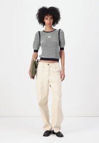 Top a righe lavorato a maglia con maniche a sbuffo in blu navy e bianco, abbinato a pantaloni crema a vita alta e scarpe nere. Porta una borsa verde.