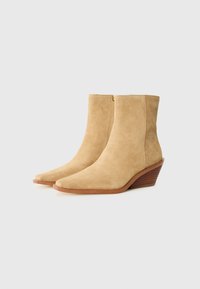 Stivaletti alla caviglia in suede beige con tacco a zeppa, punta affusolata e cerniera laterale. Presentano una base testurizzata in legno marrone.