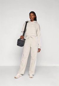 Μπεζ φούτερ με κορδόνι και κοντή σχεδίαση, σε συνδυασμό με μπεζ παντελόνια φόρμας που διαθέτουν λευκές πλαϊνές ρίγες. Μαύρη τσάντα χιαστί ως αξεσουάρ.