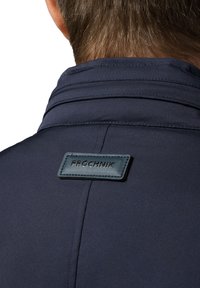 Granatowa kurtka o gładkiej fakturze, z kołnierzem i naszytą skórzaną metką z napisem "PROCHNIK" z tyłu.