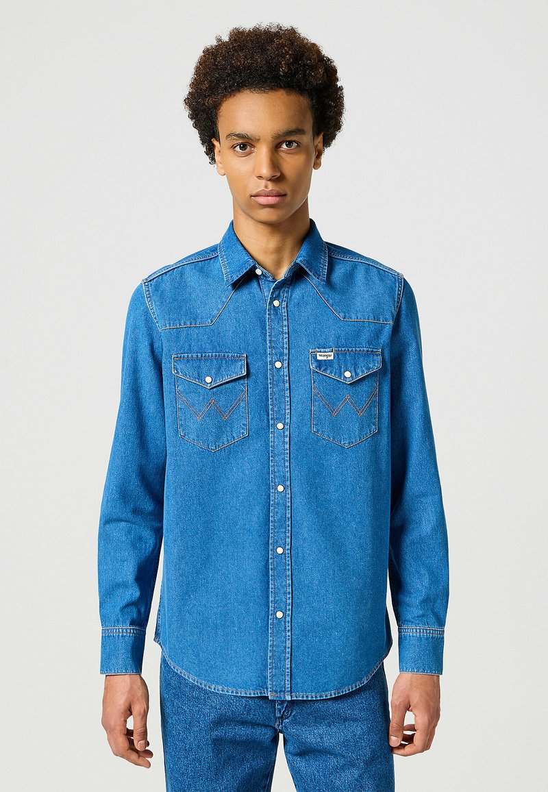 Camicia in denim blu con chiusura a bottoni a pressione, due tasche sul petto e cuciture a contrasto. Maniche lunghe con polsini a bottone, design classico western.