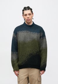 Πλεκτό πουλόβερ με διαβαθμισμένο σχέδιο σε σκούρο πράσινο, ναυτικό μπλε, γκρι και μαύρο. Διαθέτει ριμπ γιακά και άνετη εφαρμογή.