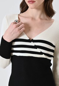 Abito lavorato a maglia con profondo scollo a V, righe orizzontali bianche e nere, e texture a coste, con maniche lunghe e silhouette aderente.