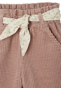 Corduroy pants in dusty pink with a textured ribbed design. Features a cream fabric belt with a floral pattern, waist tie, and front slit.