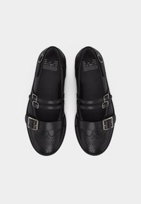 Μαύρα δερμάτινα brogue παπούτσια με διπλές λουριά με αγκράφες και διακοσμητικά διάτρητα μοτίβα, φωτογραφημένα από πάνω σε λευκό φόντο.
