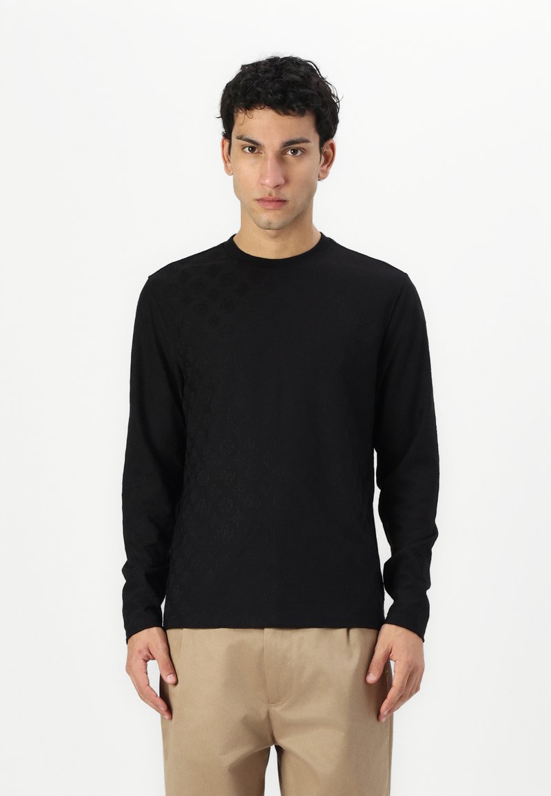 Black long-sleeve shirt featuring a textured pattern on one side, round neck design, made of soft fabric, paired with beige trousers.