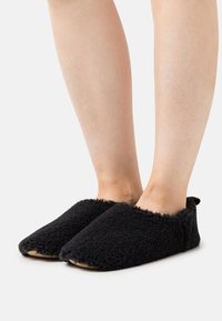 Black, fluffy slippers with a soft texture, closed-toe design, and no visible fastenings. Natural-colored soles and a rounded shape.