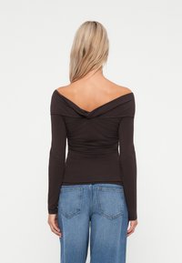 Pruun off-shoulder pikkade varrukatega topp keeratud seljaga; vormiv tekstuur ja pehme, veniv materjal; koos heledate pesupükstega.