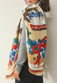 Värvikas mustriga sall siniste ja punaste kujundustega kreemika taustaga, valmistatud pehmest ja kergest kangast. Servad on narmendunud.