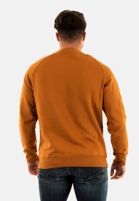 Sudadera de cuello redondo naranja con puños y dobladillo acanalados, hecha de una tela suave. La vista trasera muestra una textura lisa y una silueta ajustada.