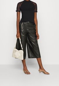 Černý top s krajkovými krátkými rukávy, široké kožené kalhoty černé barvy, bílé korálkové kabelky a páskové sandály na podpatku s jemnými ozdobami.