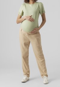 Haut ajusté vert menthe avec manches bouffantes et bordure en broderie anglaise, associé à un pantalon ample beige et des baskets blanches, adapté pour les vêtements de maternité.