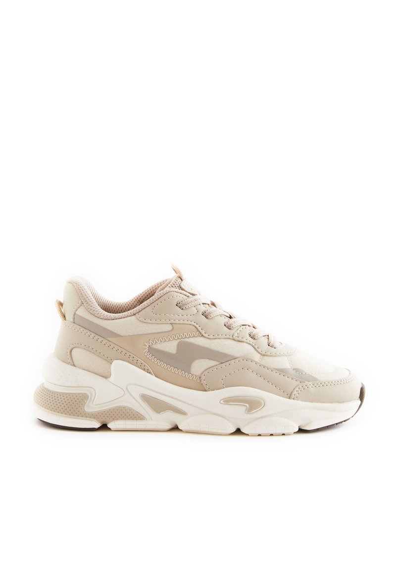 Zapatilla atlética beige que presenta una mezcla de materiales suaves y texturizados, punta redondeada, suela gruesa y diseño de cordones con acentos sutiles.