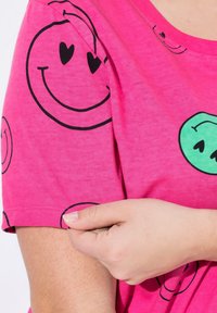 Camiseta rosa de mangas cortas hecha de tela suave, que presenta patrones de caras sonrientes negras y verdes en el frente y las mangas.