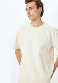 Crème kleurige t-shirt met korte mouwen in een zachte stof, met een geribbelde ronde hals en een rechte pasvorm. Heeft zijsplitten aan de zoom.