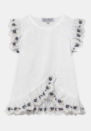 Camiseta blanca con mangas de volantes, presenta bordados florales en azul marino y bordes festoneados. Línea del dobladillo asimétrico con tejido texturizado.