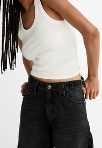Witte geribbelde tanktop gecombineerd met zwart high-waisted denim broek met zijzakken en knoopsluiting, met een ontspannen pasvorm.