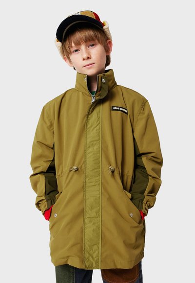 Grüne und gelbe Parka-Jacke mit Reißverschluss, Zugkordel im Saum, zwei Seitentaschen und einem Logo-Patch auf der Brust. Weiche Textur.