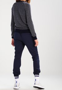 Navy sweater with white polka dots, ribbed cuffs, and hem. Paired with navy joggers, elastic at ankles, and white sports shoes with blue accents.