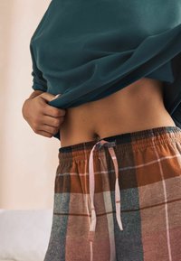 Teal oversized sweatshirt stikket ned i brune og gråternet loungewear shorts med en lyserød snor. Glat tekstur og elastisk talje synlig.