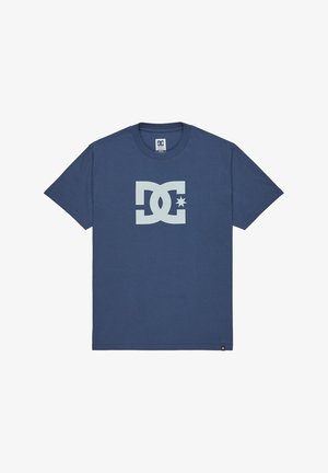 Niebieska koszulka z krótkim rękawem z dużym białym logo DC i gwiazdą umieszczoną na środku przodu, okrągły dekolt oraz mała czarna metka DC na dolnym suwaku.