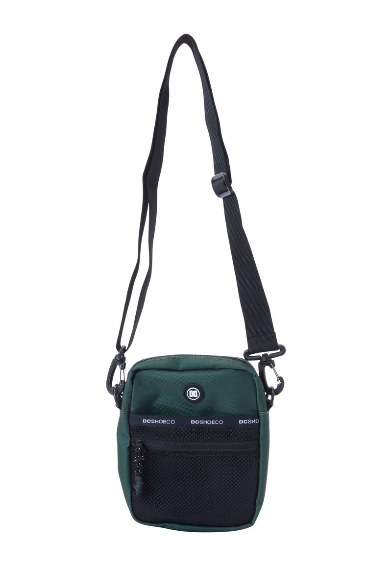 Zelená crossbody taška vyrobená z nylonu, s predným zipsovým vreckom s sieťovinou, logom a nastaviteľným čiernym popruhom. Kompaktný obdĺžnikový tvar.