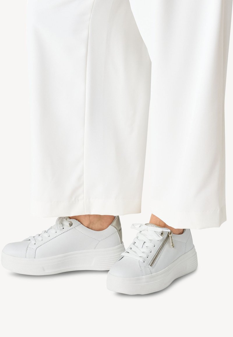 Sneaker bianco con tomaia in pelle liscia, design con lacci, dettagli argentati e zip laterale. La suola è spessa e strutturata.