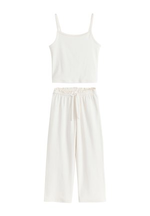Top corto blanco sin mangas con tirantes finos combinado con pantalones blancos sueltos de talle alto con cintura elástica y cordón.