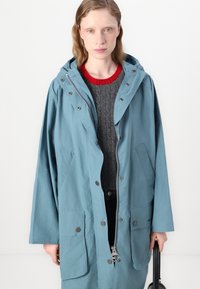 Light blue oversized jacket with a hood, silver zipper, snap buttons, and front pockets, layered over a textured gray sweater.