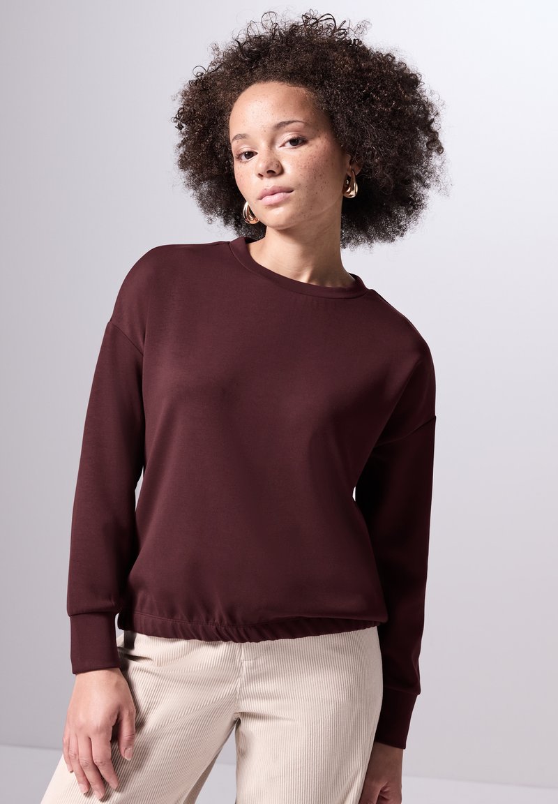 Bordeaux sweatshirt met lange mouwen, geribbelde ronde hals en elastische taille. Gecombineerd met beige corduroy broek, met een gladde textuur.