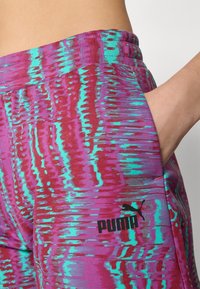 Leggings de atletismo Puma com um padrão vibrante em púrpura e teal, apresentando uma textura suave, cintura elástica e detalhe de bolso lateral.