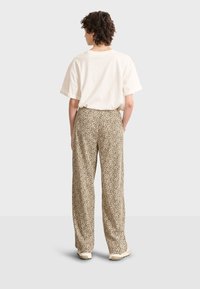 Pantaloni a gamba larga beige con stampa leopardata nera, abbinati a una t-shirt morbida di colore crema. Tessuto morbido, design casual.
