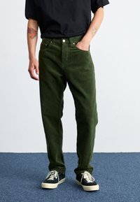 Zelené kordové kalhoty s viditelnými žebry, rovný střih, pět kapsových design, stříbrné zapínání na knoflík, v kombinaci s černými plátěnými botami.