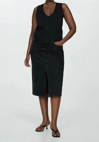 Czarna kamizelka i spódnica dżinsowa do kolan. Kamizelka ma dekolt w serek i zapięcie na guziki; spódnica ma rozcięcie z przodu i kieszenie.